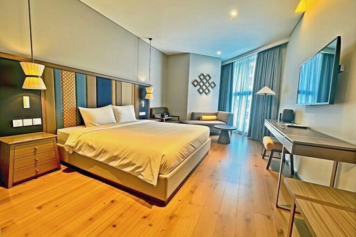 A modern hotel room with a large bed, a desk, a chair, and a small table.