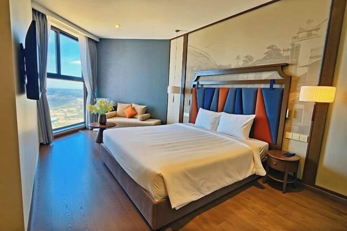 A hotel room with a large bed, a sofa, a small table, and a view of the city.