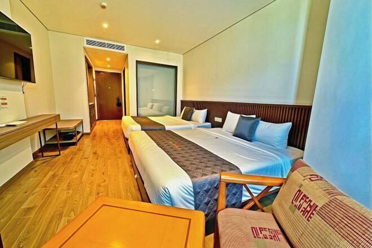 A hotel room with two beds, a desk, a chair, and a TV.