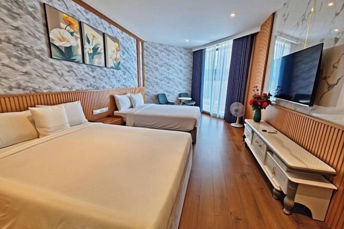 A hotel room with two beds, a TV, a desk, and a large window.