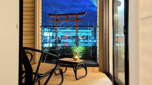 En balkon med udsigt over en by om natten, med et traditionelt japansk torii-helligsted og moderne bygninger.
