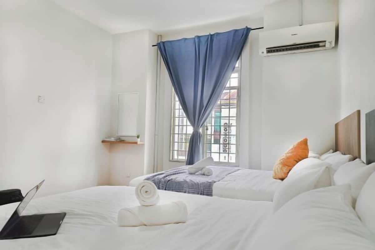 Habitación de hotel con dos camas, una computadora portátil sobre una cama y una ventana con cortinas azules.