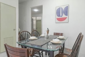 A dining area with a glass table, wooden chairs, and a wall-mounted abstract painting. - Damansara Damai 9Pax 4 Rooms (Petaling Jaya)
