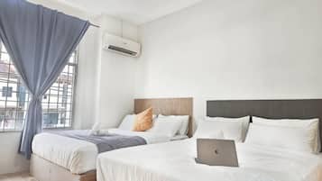 Quarto de hotel com duas camas, um laptop sobre uma delas e um aparelho de ar condicionado na parede.