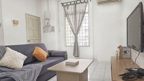 A living room with a sofa, a coffee table, a TV, and a window with curtains. - Damansara Damai 9Pax 4 Rooms (Petaling Jaya)