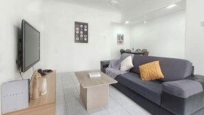 A modern living room with a flat-screen TV, a sofa with cushions, a coffee table, and a wall-mounted shelf. - Damansara Damai 9Pax 4 Rooms (Petaling Jaya)