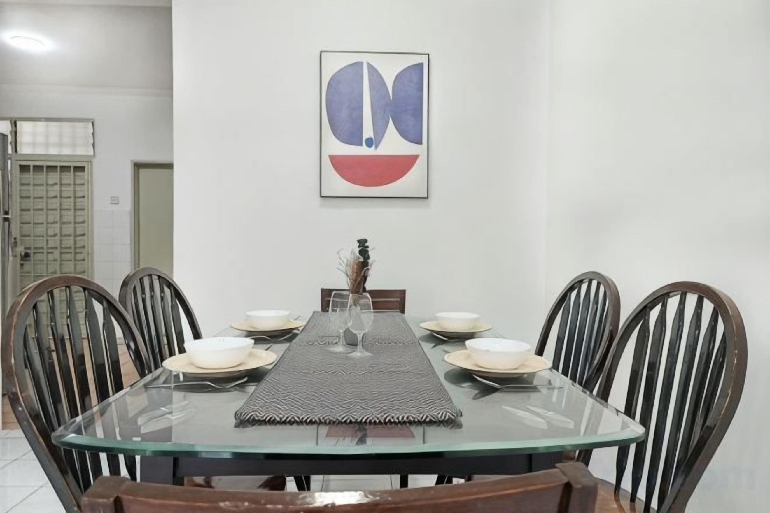 Une table à manger avec un plateau en verre, entourée de chaises en bois, mise avec des assiettes et un verre.