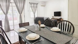 A dining area with a table set for four, chairs, a vase with flowers, and a television in the background. - Damansara Damai 9Pax 4 Rooms (Petaling Jaya)