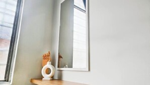A room with a wooden shelf, a white vase, and a mirror reflecting a window. - Damansara Damai 9Pax 4 Rooms (Petaling Jaya)