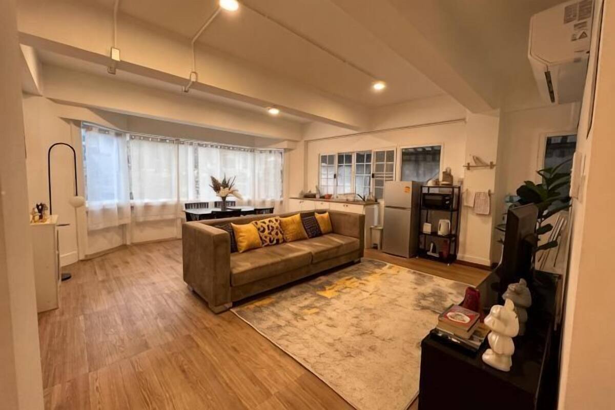 A modern living room with a sofa, a rug, and a kitchen area in the background.