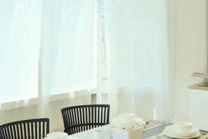 A dining area with a table set for two, chairs, and a window with sheer curtains. - Hidden Gems in China Town, 2 Bedrooms (Bangkok)