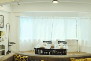 A dining area with a table set for four, a sofa with cushions, and a window with curtains. - Hidden Gems in China Town, 2 Bedrooms (Bangkok)