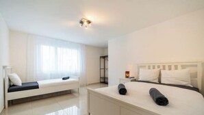Una habitación de hotel moderna con una cama grande, un sofá más pequeño y una mesita de noche con lámpara.