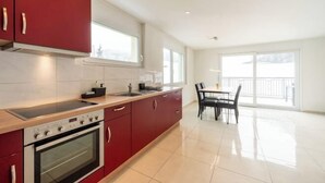 Una cocina moderna con armarios rojos, horno empotrado y un comedor con mesa y sillas.