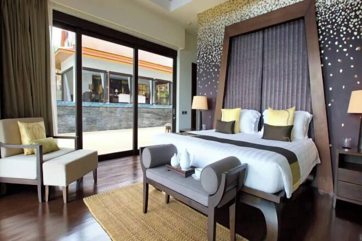 A modern hotel room with a large bed, a sofa, a desk, and a view of a pool and building.