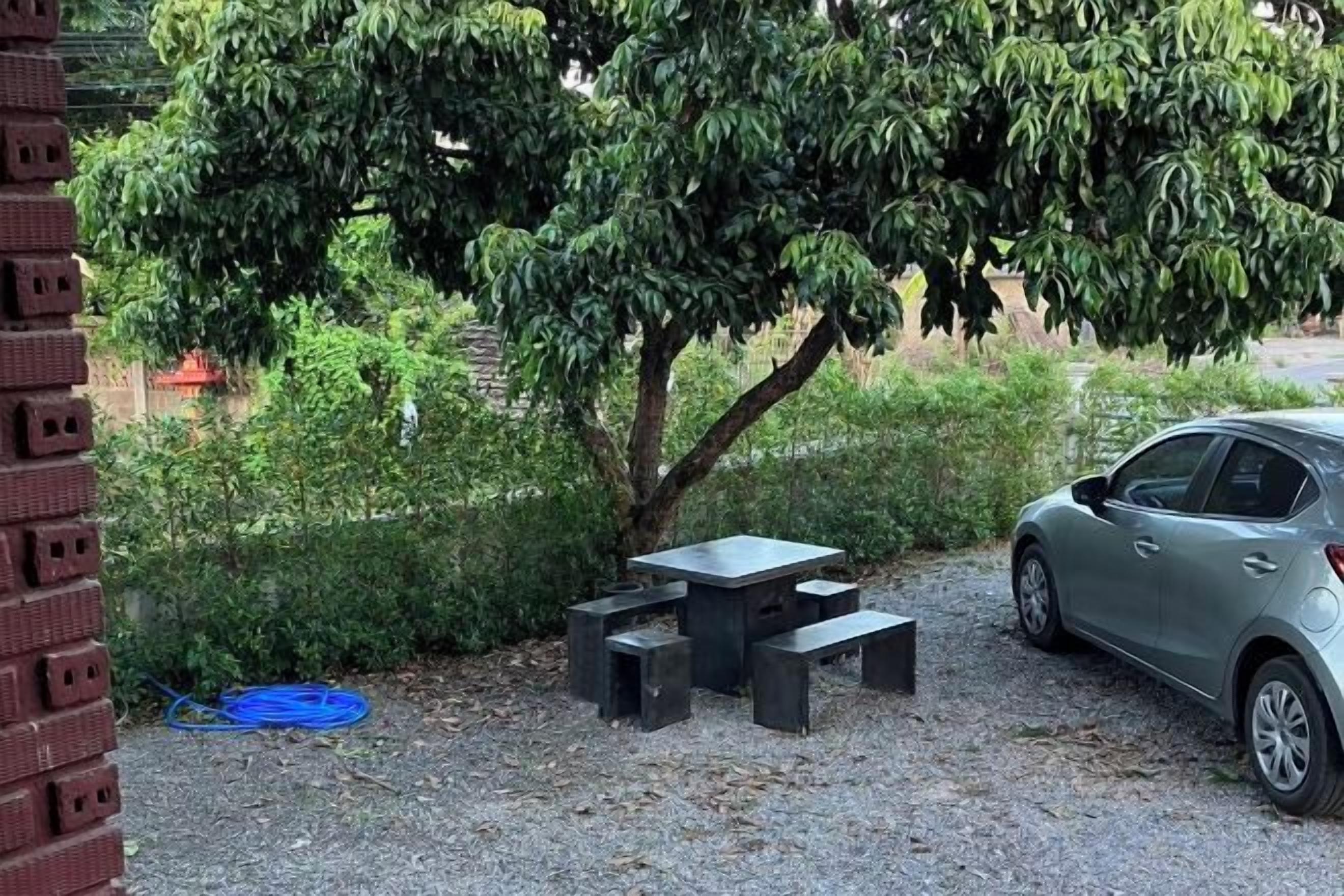 A gravel patio with a table and benches, a car, and a tree.