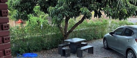 A gravel patio with a table and benches, a car, and a tree.