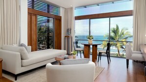 Ein modernes Wohnzimmer mit großem Fenster mit Blick auf den Ozean, einem weißen Sofa, einem Esstisch mit Stühlen und einem kleinen Beistelltisch.