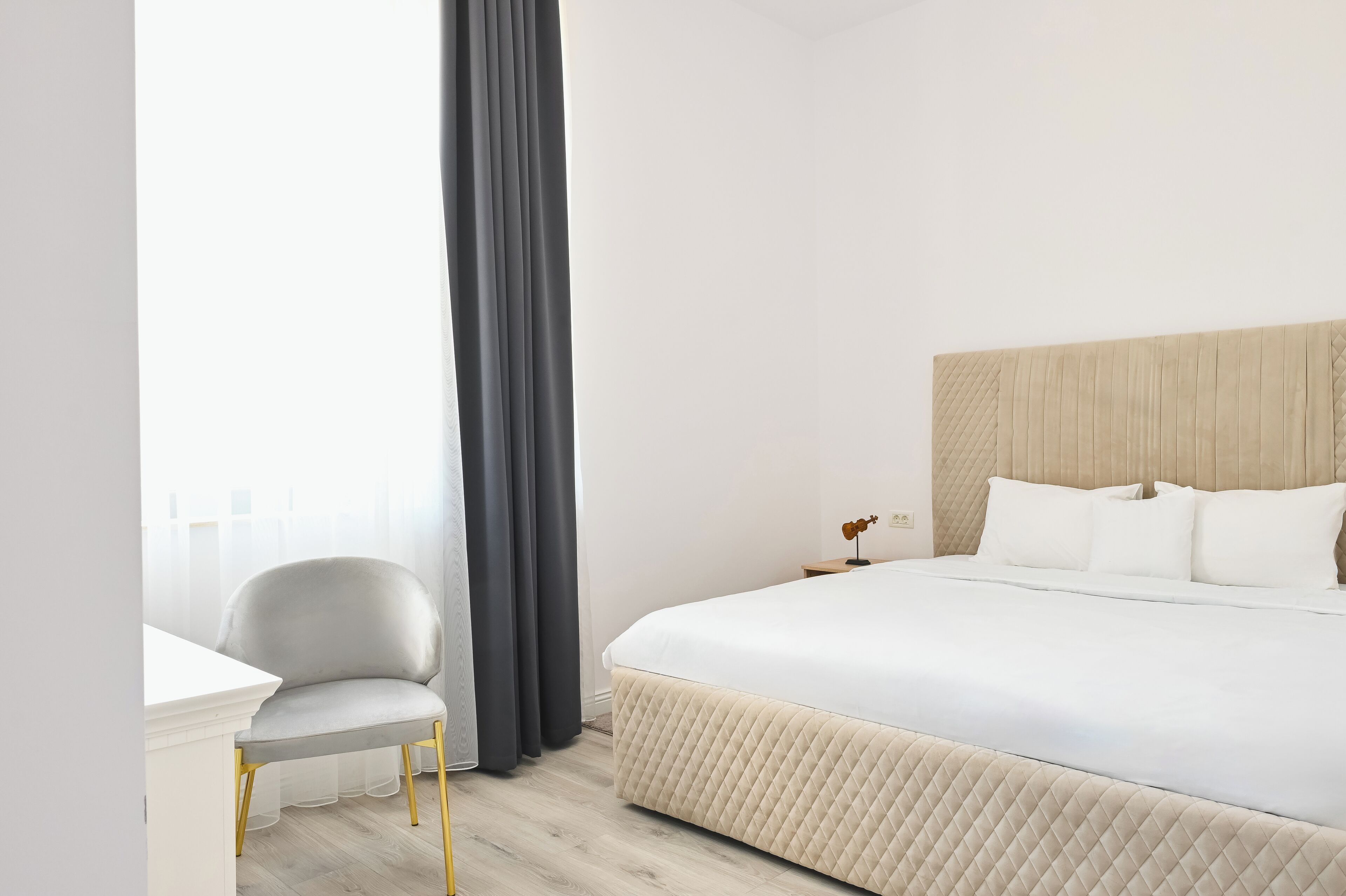 Ein Hotelzimmer mit Bett, Sessel, Nachttisch und einem Vorhangfenster.