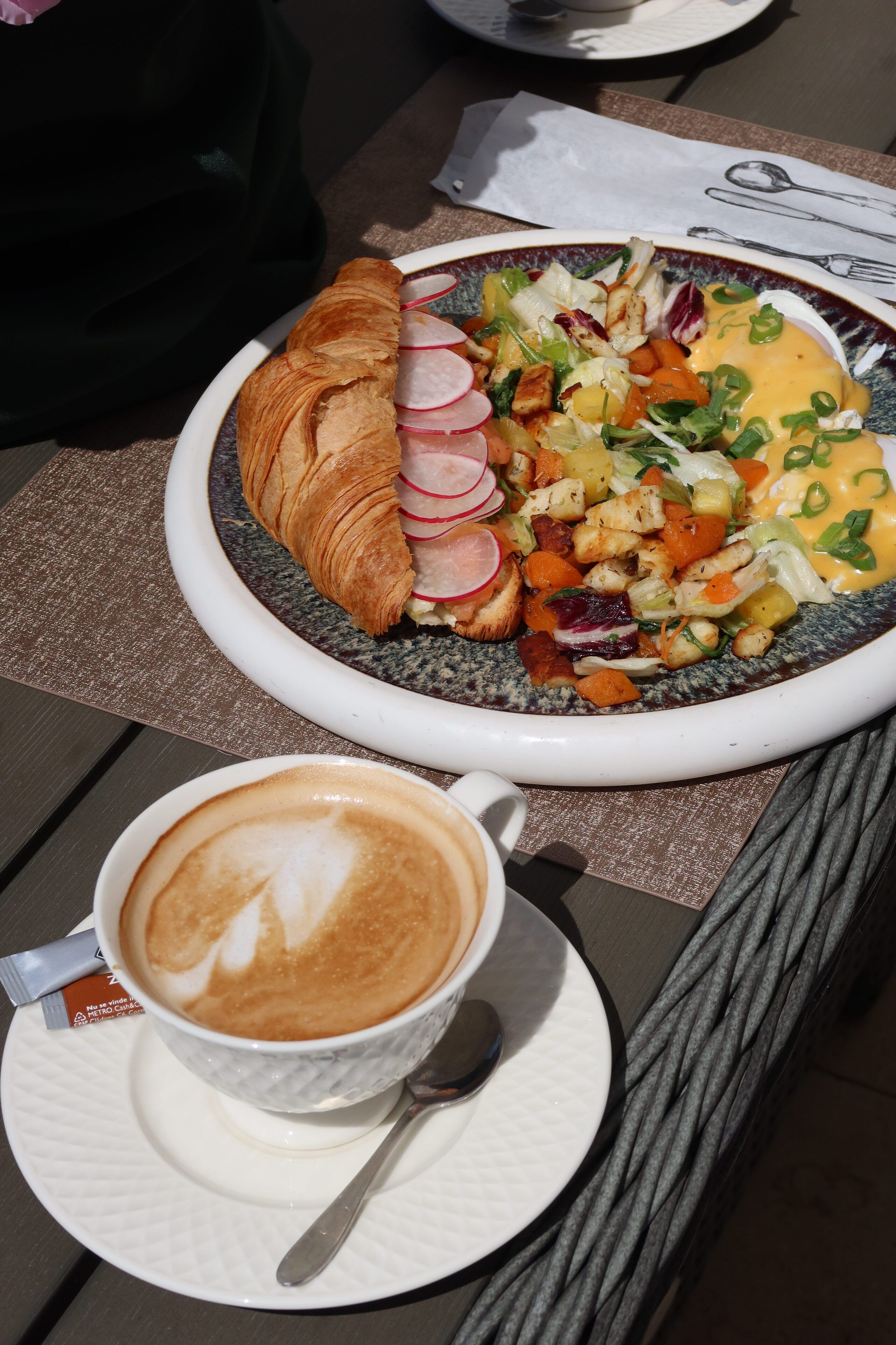 A meal consisting of a croissant, a salad with various vegetables, and a cup of coffee on a table.