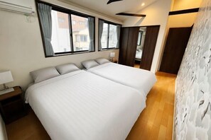 Een hotelkamer met twee bedden, een nachtkastje, een raam met gordijnen en een houten vloer.