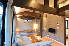 A modern living room with a stone wall, wooden beams, a sofa, a coffee table, and a TV mounted on the wall. - KandoStay Asakusa East Terrace (Tokyo)