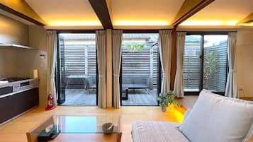A modern living room with a sofa, a glass coffee table, and a view of an outdoor patio area with a table and chairs.