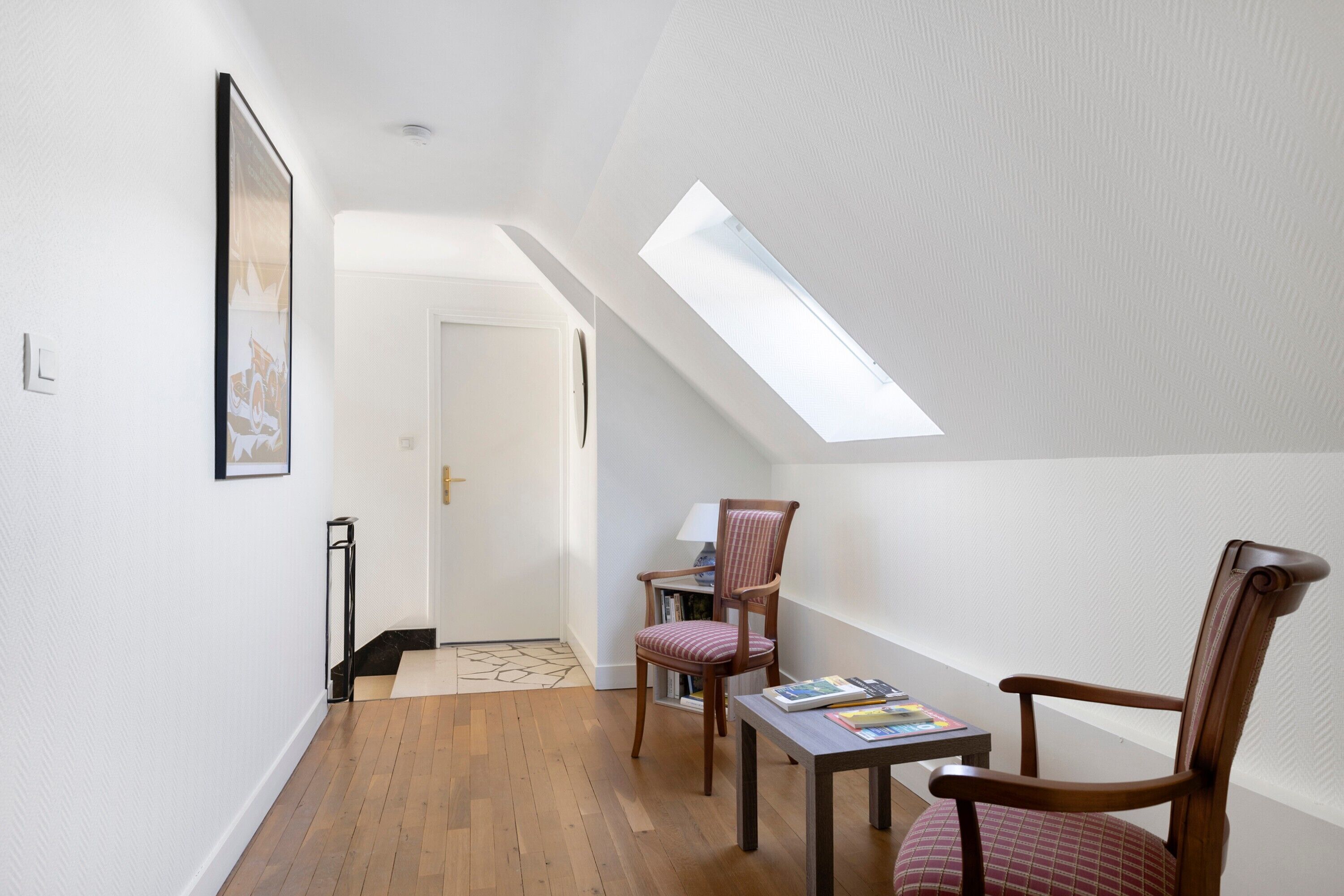 Une pièce dotée d’une lucarne, d’un plancher en bois, d’une chaise, d’une table et d’un tableau encadré au mur.