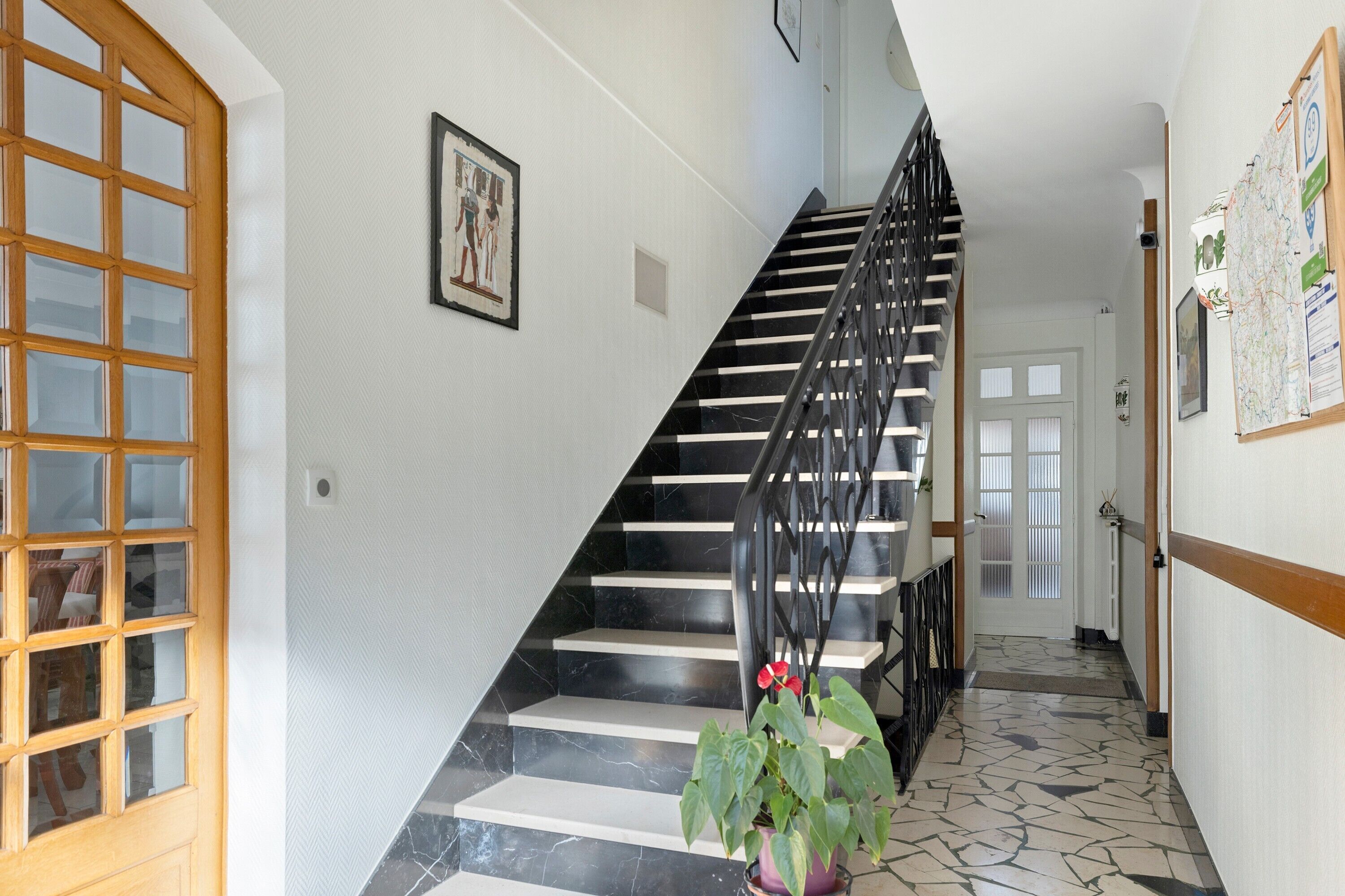 A staircase with black railings, a potted plant, and a door with a window.