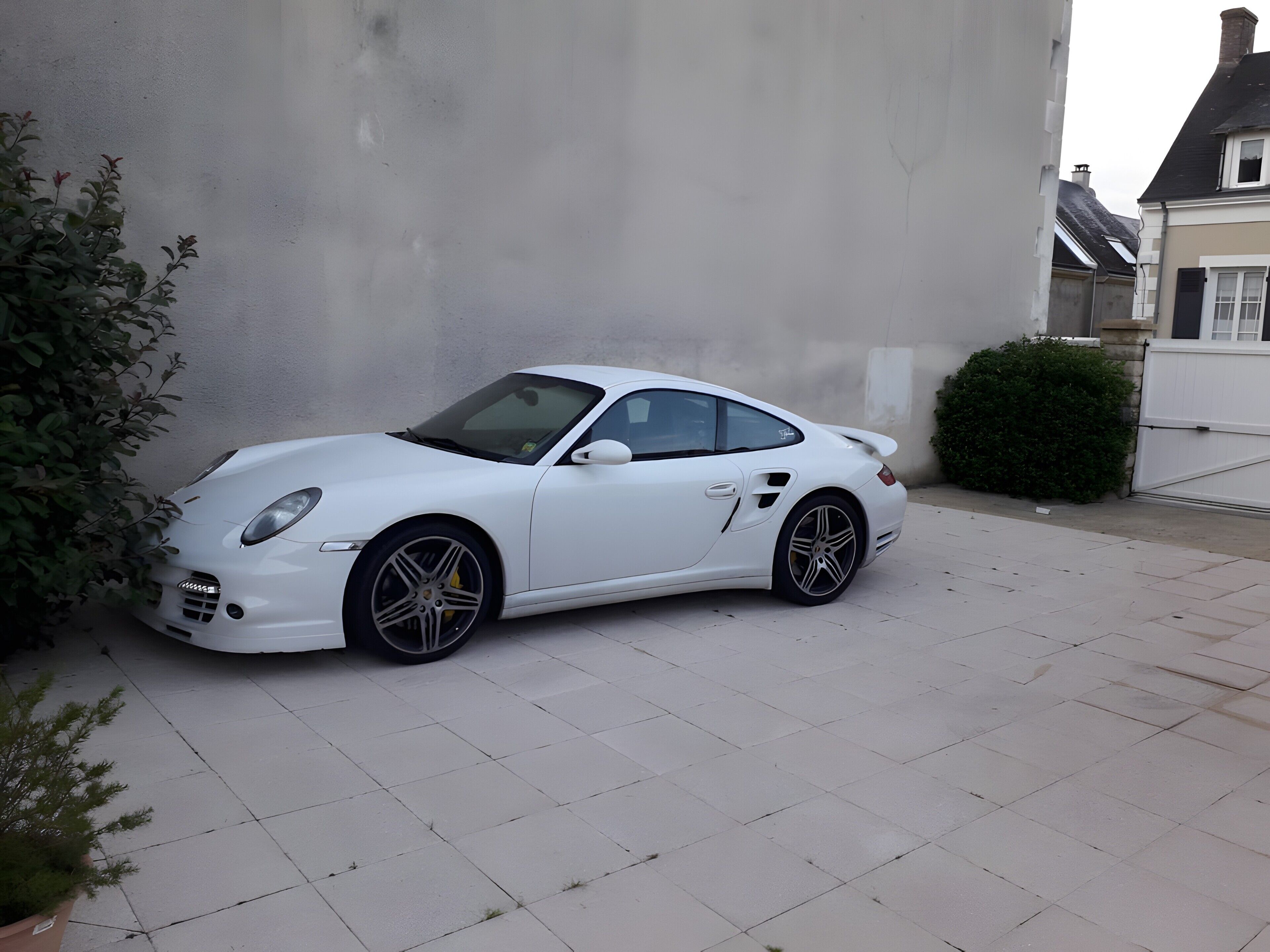 A white sports car parked on a paved driveway.