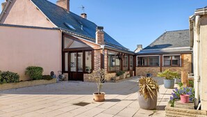 Une cour avec des plantes en pot, un bâtiment en briques et une entrée avec une porte en verre.