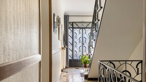 Un couloir avec un sol à motifs, une plante en pot, une rambarde en métal et une porte.