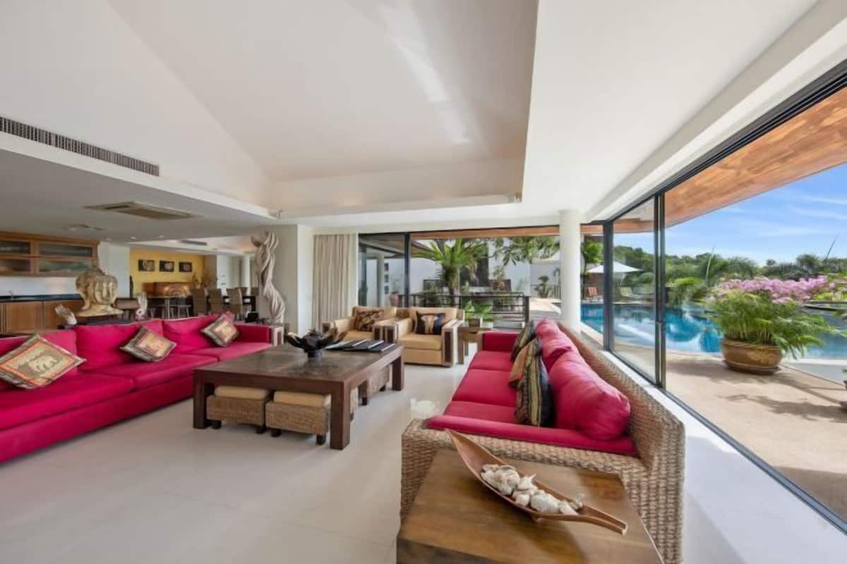 A spacious living room with a red sofa, a coffee table, and a view of a swimming pool.