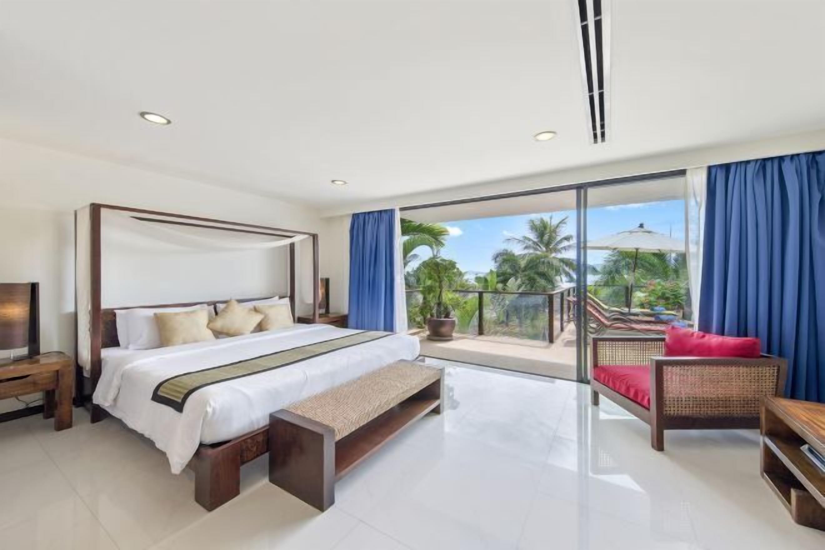 Una habitación de hotel moderna con una cama grande, un banco, un sofá y un balcón con vistas a palmeras.