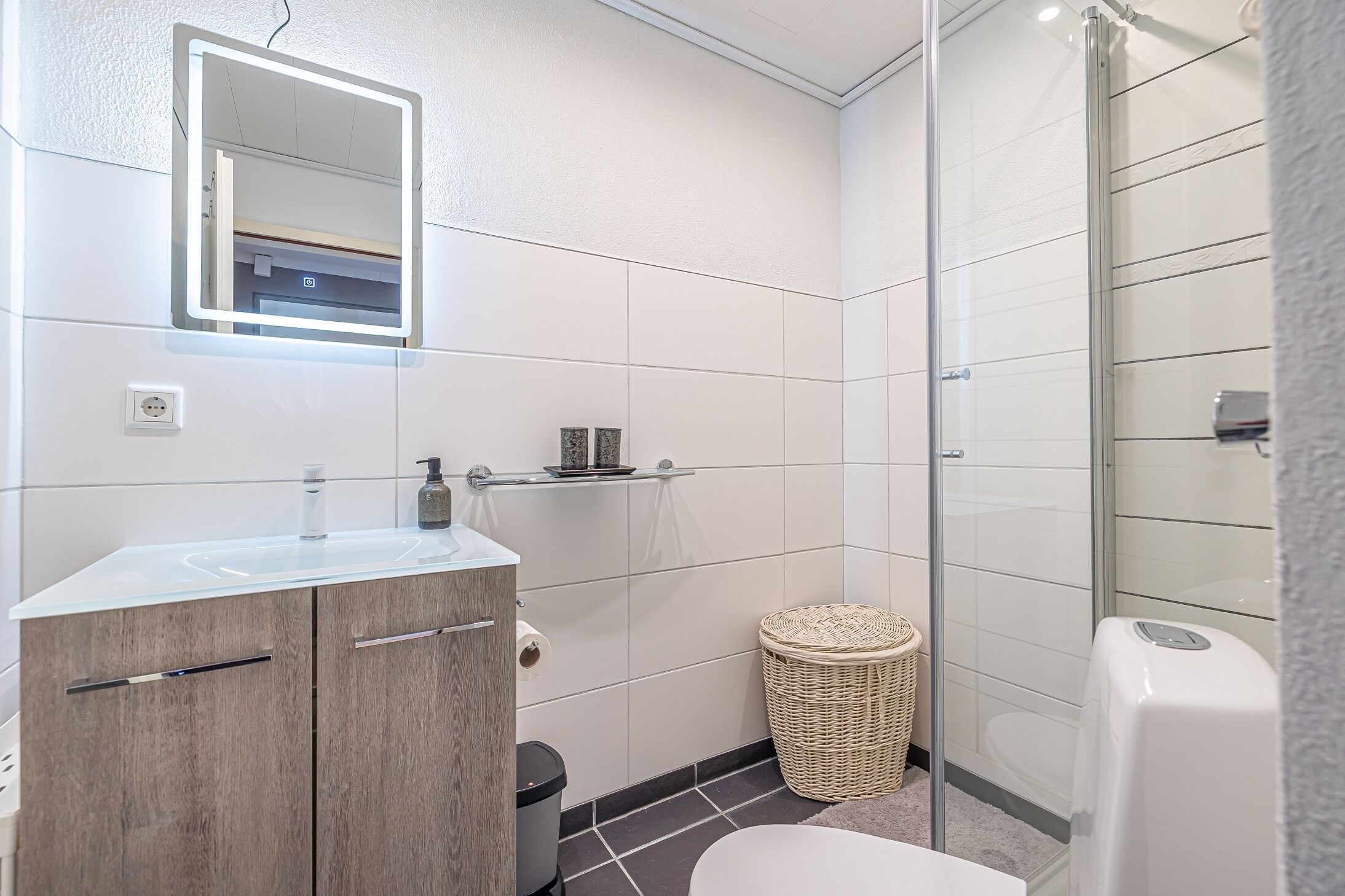 A modern bathroom with a glass shower enclosure, a wooden vanity, and a white sink.