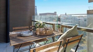 A balcony with a wooden table set for dining, a wicker basket, and a vase with flowers. - A Chic 2BR Apt Near Melbourne Uni, FREE Parking (Carlton)