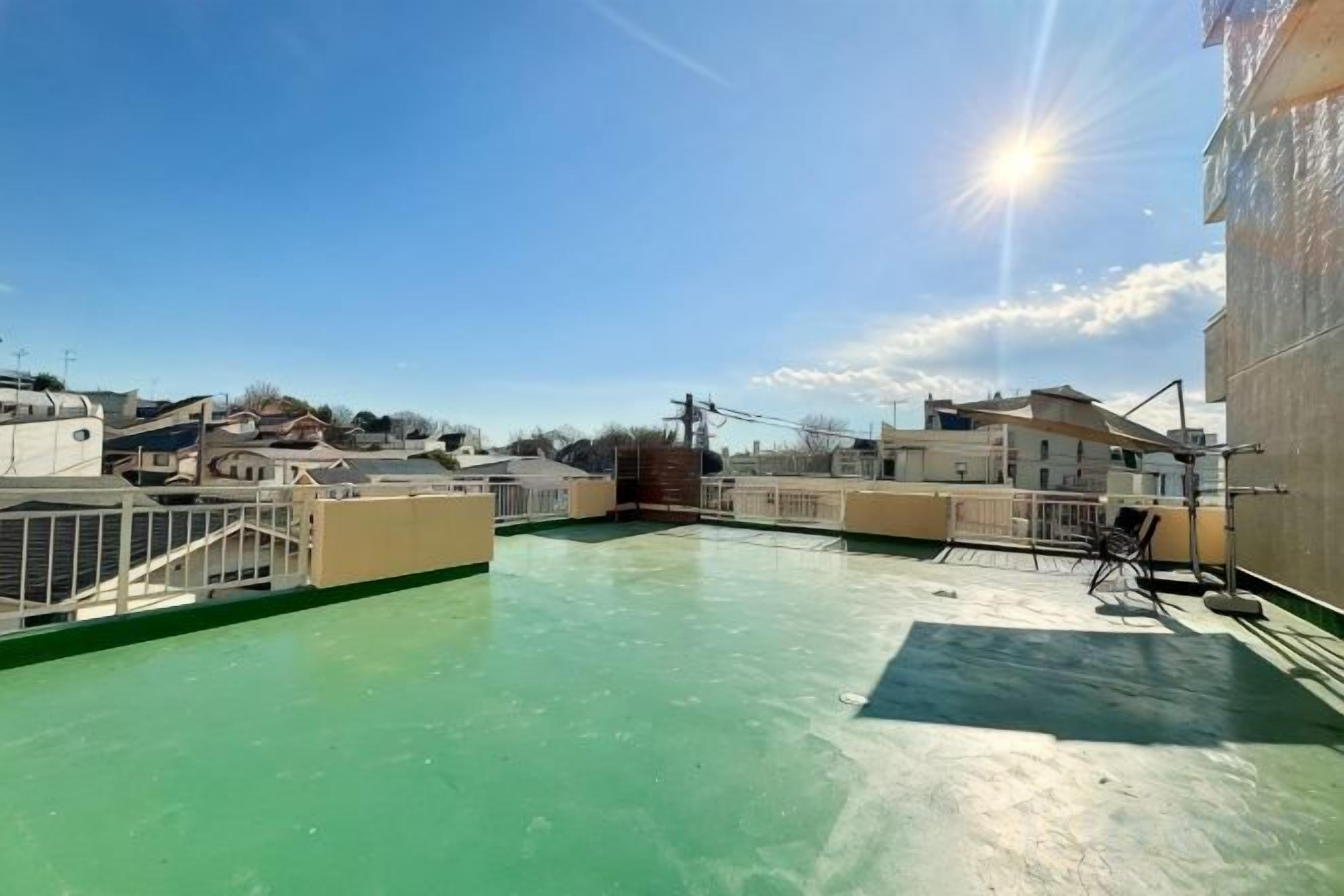 A rooftop terrace with a green floor, surrounded by buildings, under a clear sky.