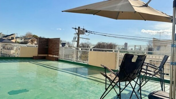 Una terraza en la azotea con piscina, una silla plegable y una sombrilla.