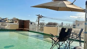 A rooftop terrace with a pool, a folding chair, and an umbrella.