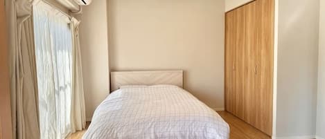 Un dormitorio con una cama, un armario de madera y un ventanal con cortinas.