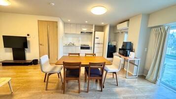 A modern kitchen with white cabinets, a dining table with chairs, a TV, and a balcony with curtains.