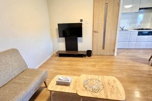 Una sala de estar con un sofá, una mesita con un bol de vidrio, un televisor de pantalla plana y una puerta que da a la cocina.