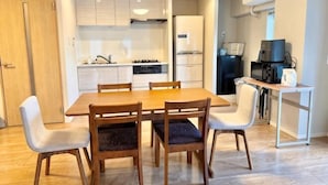 Un comedor con mesa y sillas de madera, una cocina con armarios blancos y una pequeña mesa con hervidor.