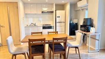 A dining area with a wooden table and chairs, a kitchen with white cabinets, and a small table with a kettle.
