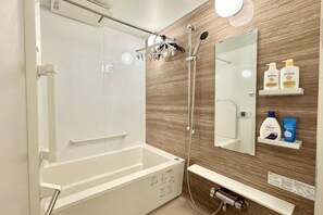 Moderni kylpyhuone, jossa on kylpyamme, suihku ja peili sekä hygieniatuotteita.