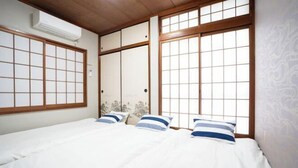 A traditional Japanese-style room with tatami flooring, sliding doors, and a bed with white bedding and striped pillows. - DAIJUN HOTEL (Naha)
