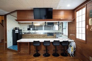 A modern kitchen with a marble countertop and bar stools, wooden cabinets, and a black television mounted above the counter. - DAIJUN HOTEL (Naha)