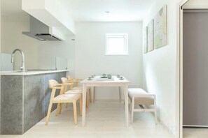 A modern kitchen with a dining area, including a table and chairs, and a small window providing natural light. - Downtown Mix (Tokyo)