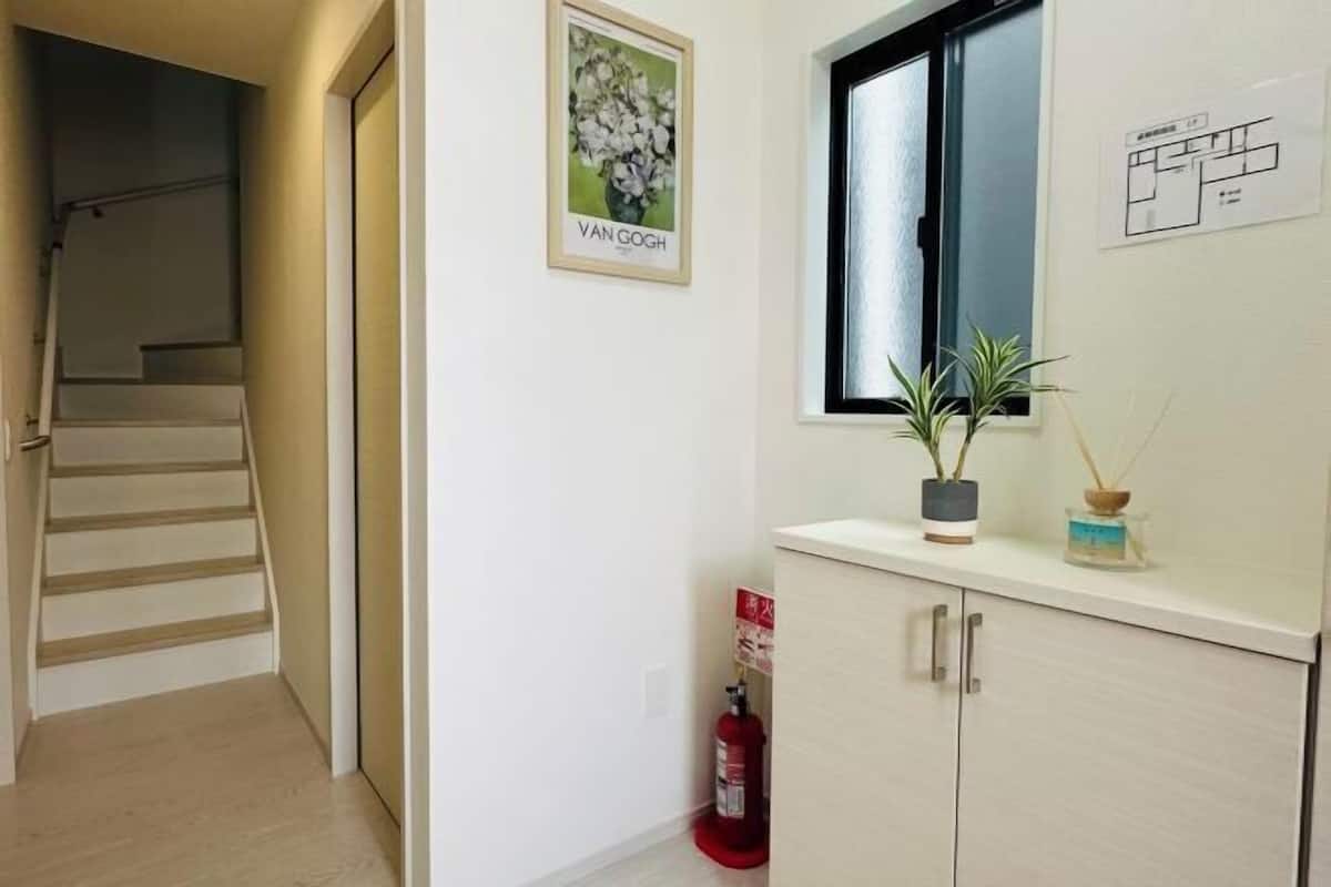 Un couloir avec un escalier, un tableau encadré représentant des fleurs, une fenêtre et un extincteur.
