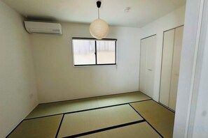 Une pièce avec un sol recouvert de tatamis, une porte coulissante, une fenêtre donnant sur un paysage agréable et une lanterne en papier suspendue.